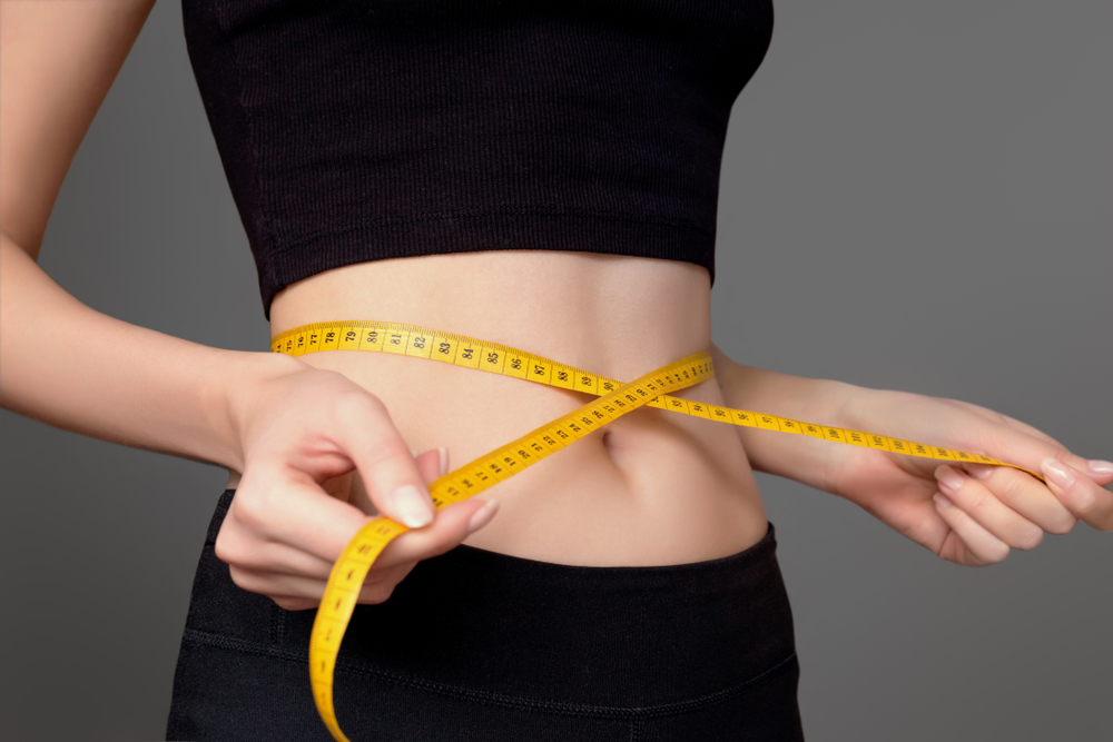 Woman measuring her waist with a tape measure after a weight loss program.