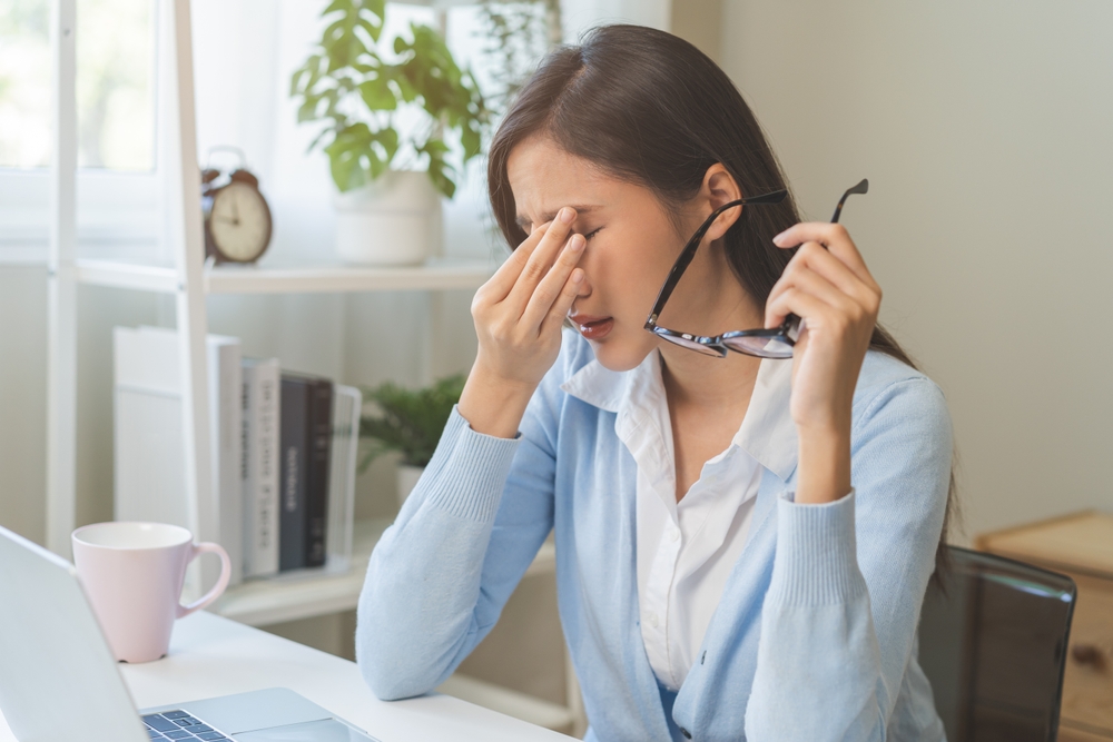 Woman experiencing fatigue and eye strain while working at a laptop, representing symptoms that may lead to lab testing.